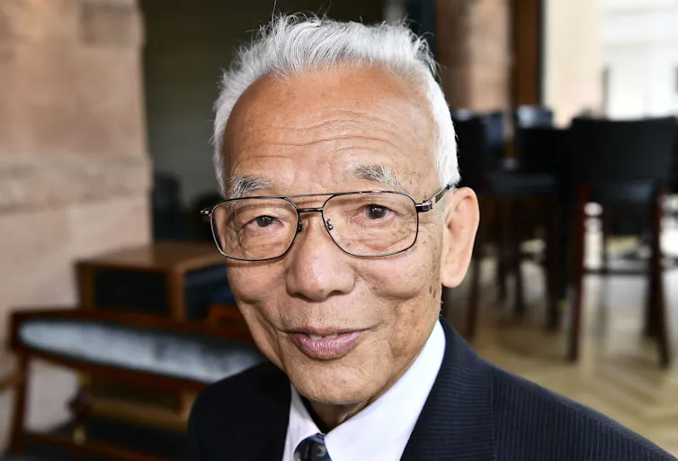 An older man smiles at the camera with an impish grin.