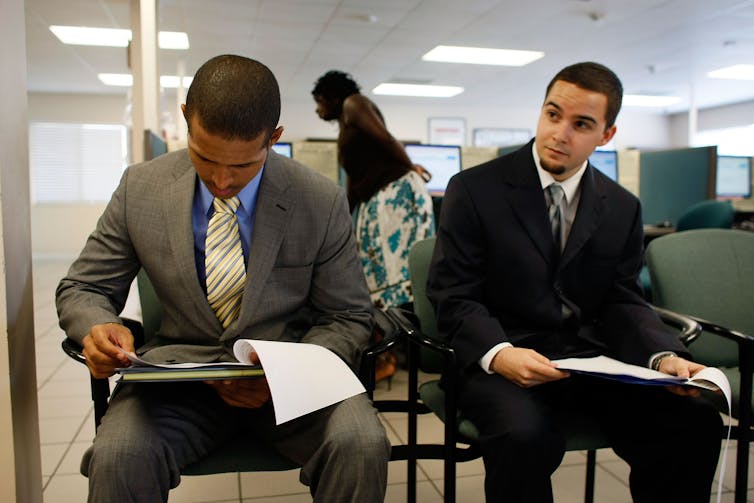Two men fill out paperwork as they wait for a job interview