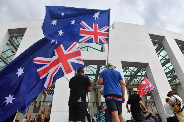 A group of people outside Canberra parliament hosue wave upside down Australian flags
