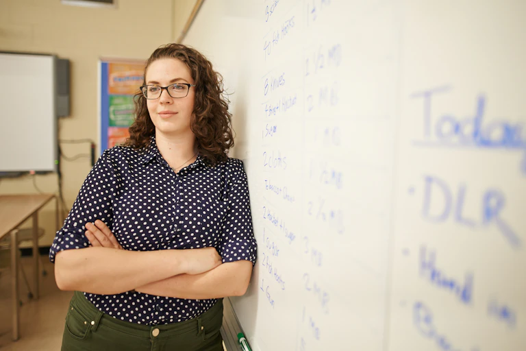 A woman leans against a whiteboard with writing on it.