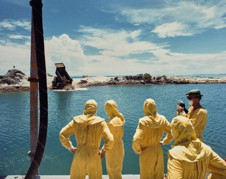 Five people in yellow protective clothing stand near the water.