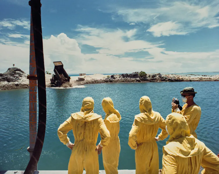 Five people in yellow protective clothing stand near the water.