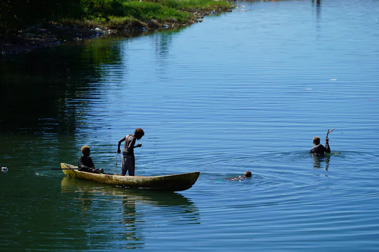 Two people on a boat and one person in the water.