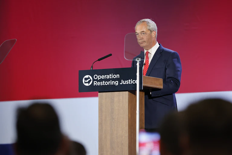 Nigel Farage standing at a podium that reads 'operation restoring justice'