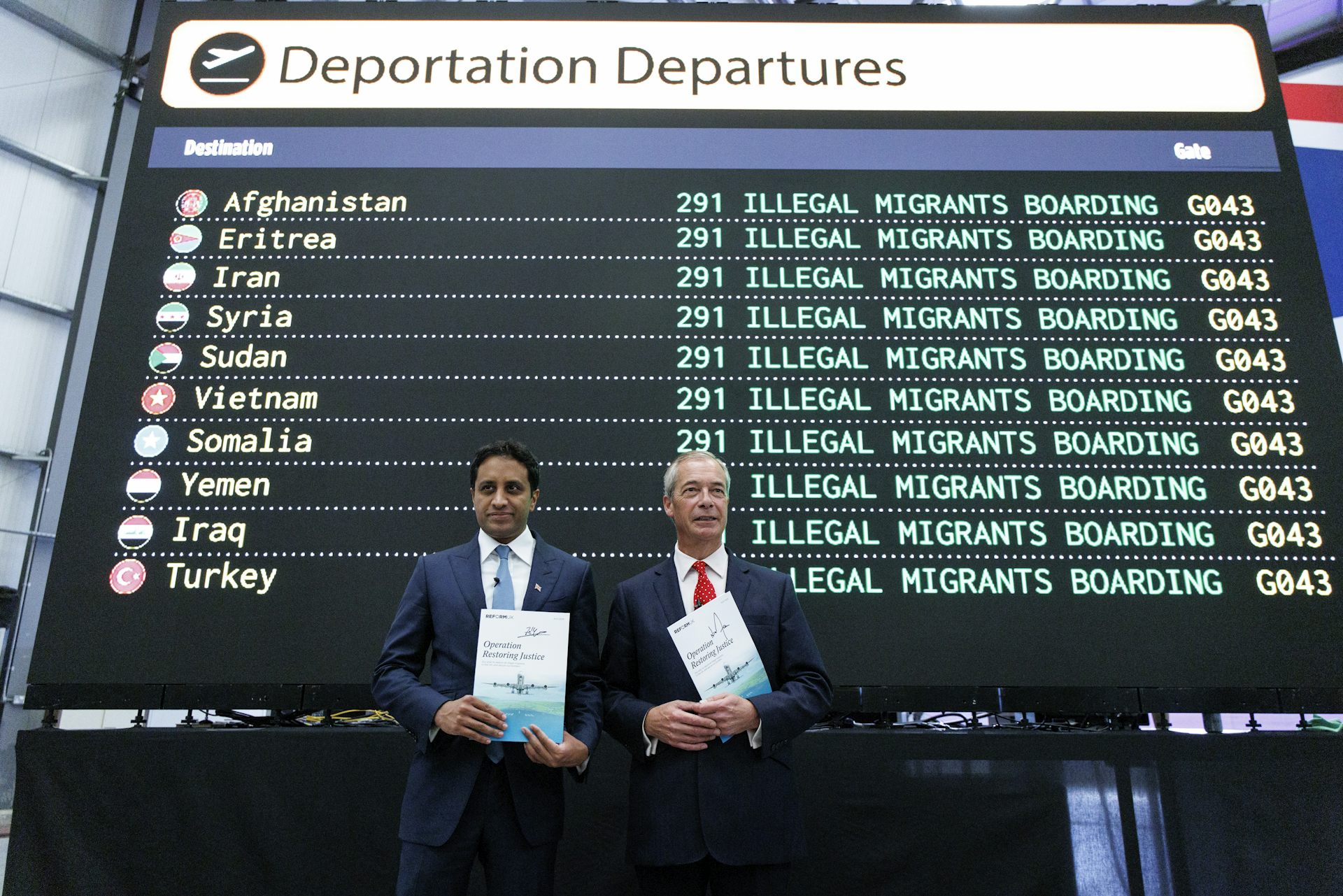 Zia Yusuf and Nigel Farage standing in front of a mock departures board that reads 'illegal migrants boarding'