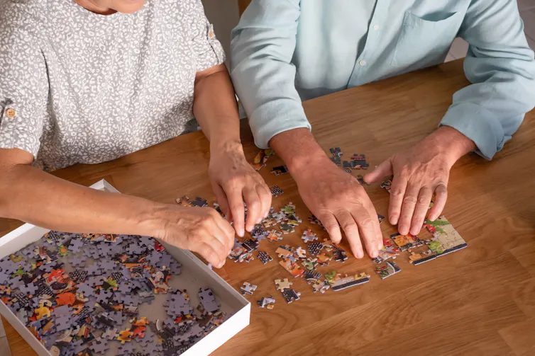 Two elderly people try to complete a puzzle.