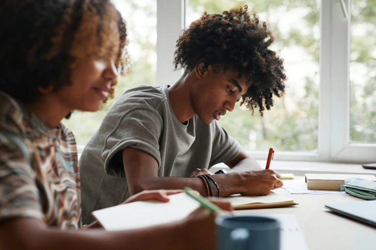 Two students at desks, one with pencil and paper.