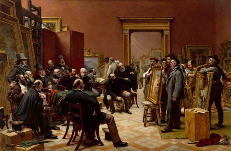 Men in Victorian European suits in a room on chairs and standing examining paintings.