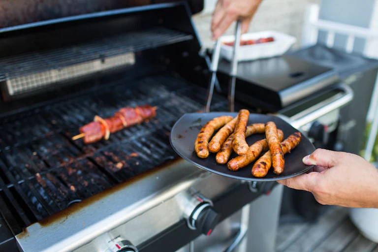 Man taking sausages off a barbecue grill.