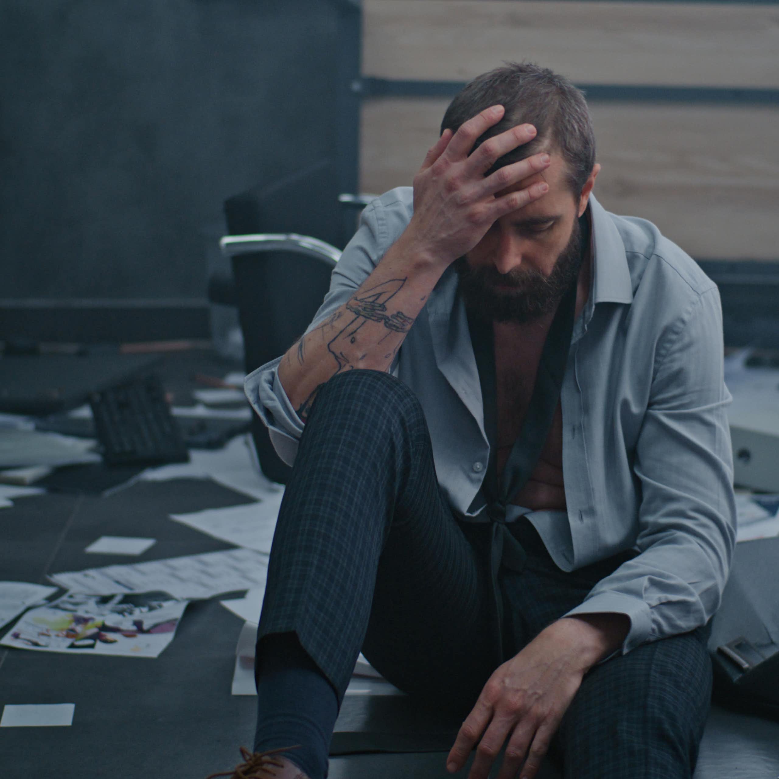 un homme au bout du rouleau dans un décor de bureau en grand désordre. l'éclairage est très très sombre