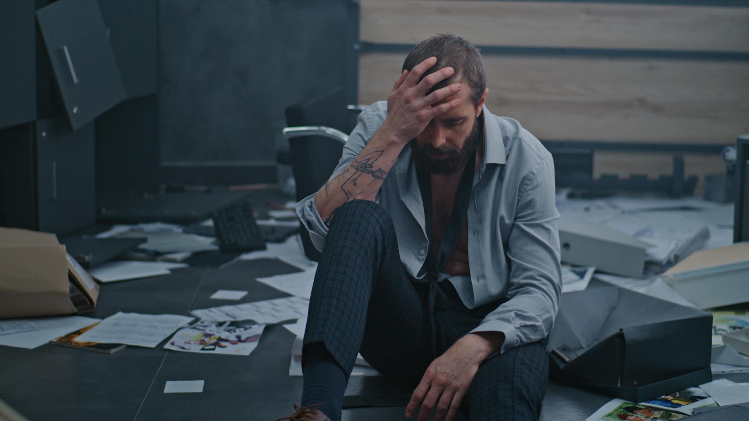 un homme au bout du rouleau dans un décor de bureau en grand désordre. l'éclairage est très très sombre