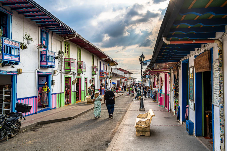 Dos personas pasean por una calle tranquila bordeada de casas coloridas.