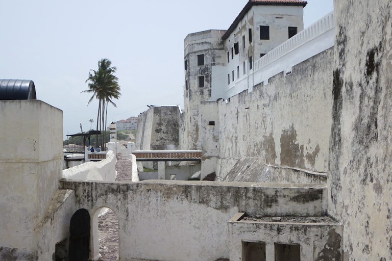 Large old wall and building with palm trees in the distance