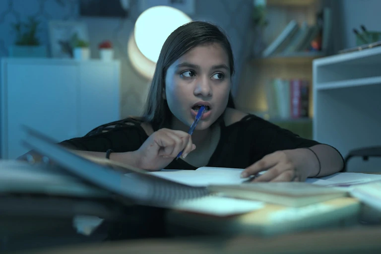 Una niña con gesto de intentar recordar algo mientras estudia en su habitación