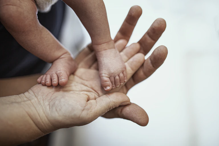 Two-week-old baby's feet rest on a man's hand and a woman's hand.