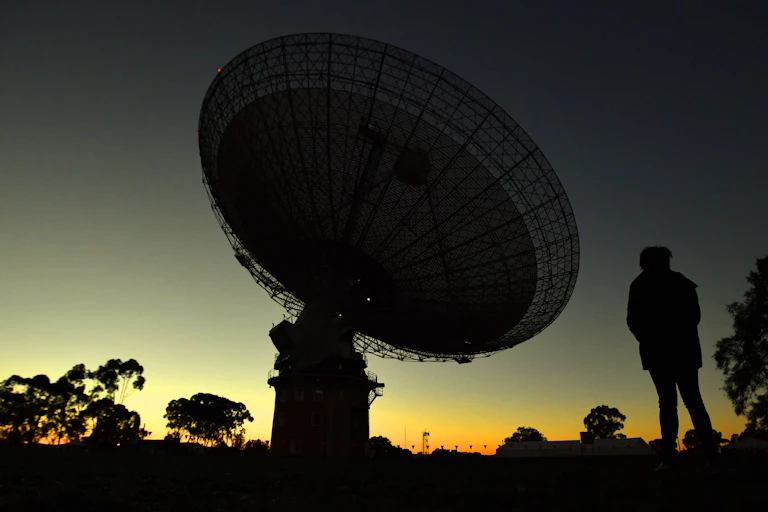 Silhouetted radio dish against a sunset sky.