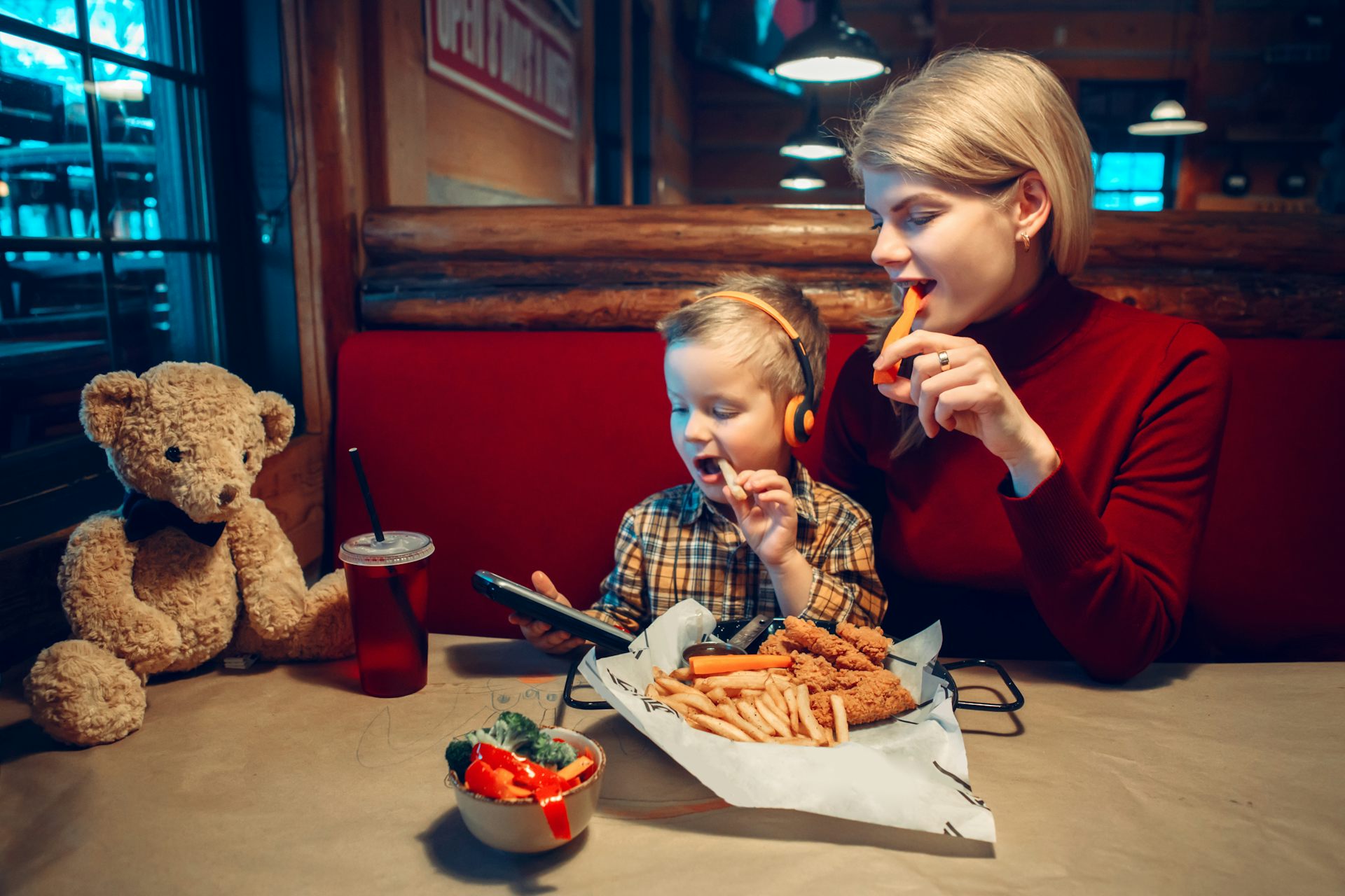 Mujer y niño comiendo en un restaurante mientras miran la pantalla de un dispositivo.