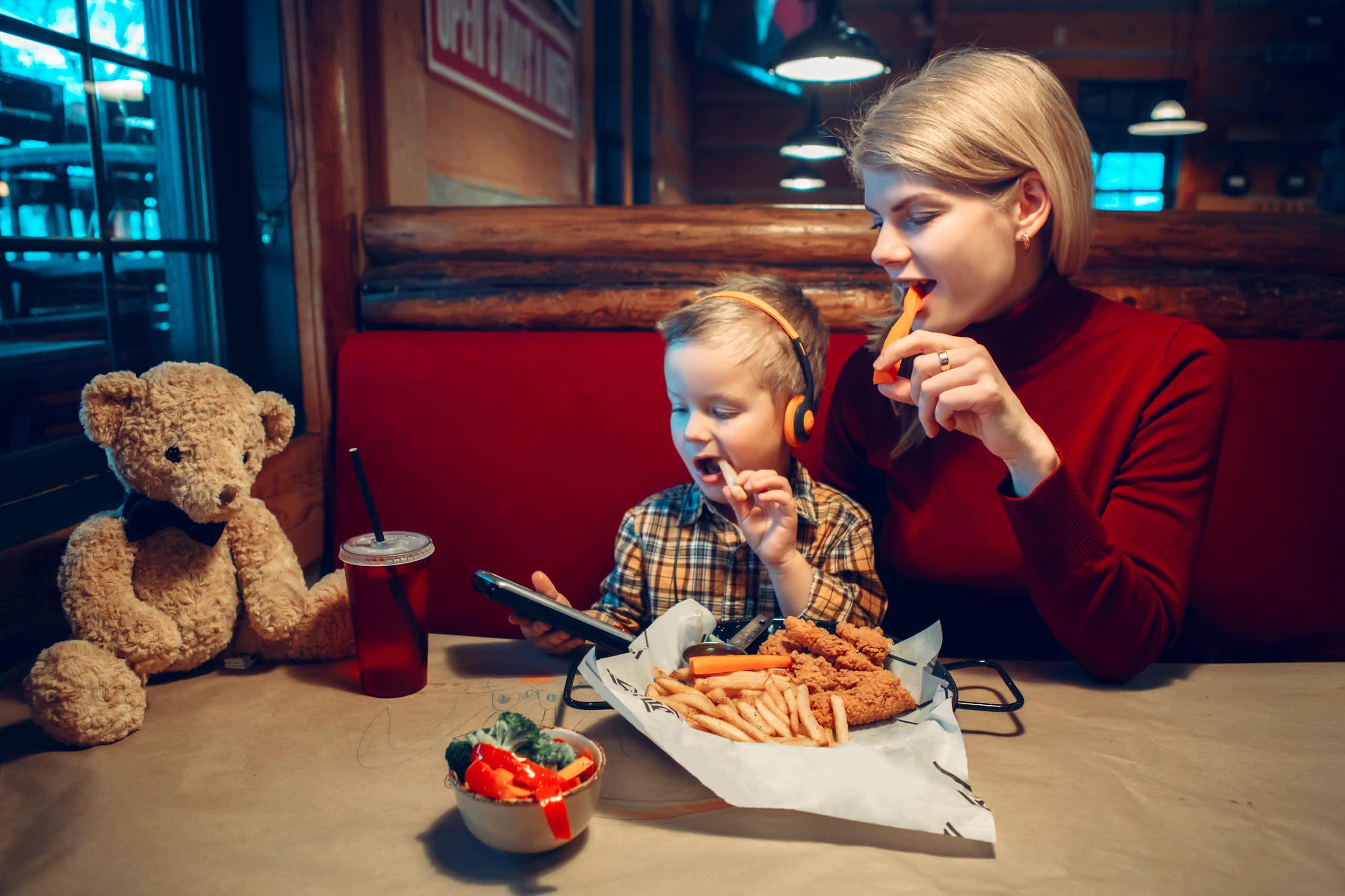 Mujer y niño comiendo en un restaurante mientras miran la pantalla de un dispositivo.