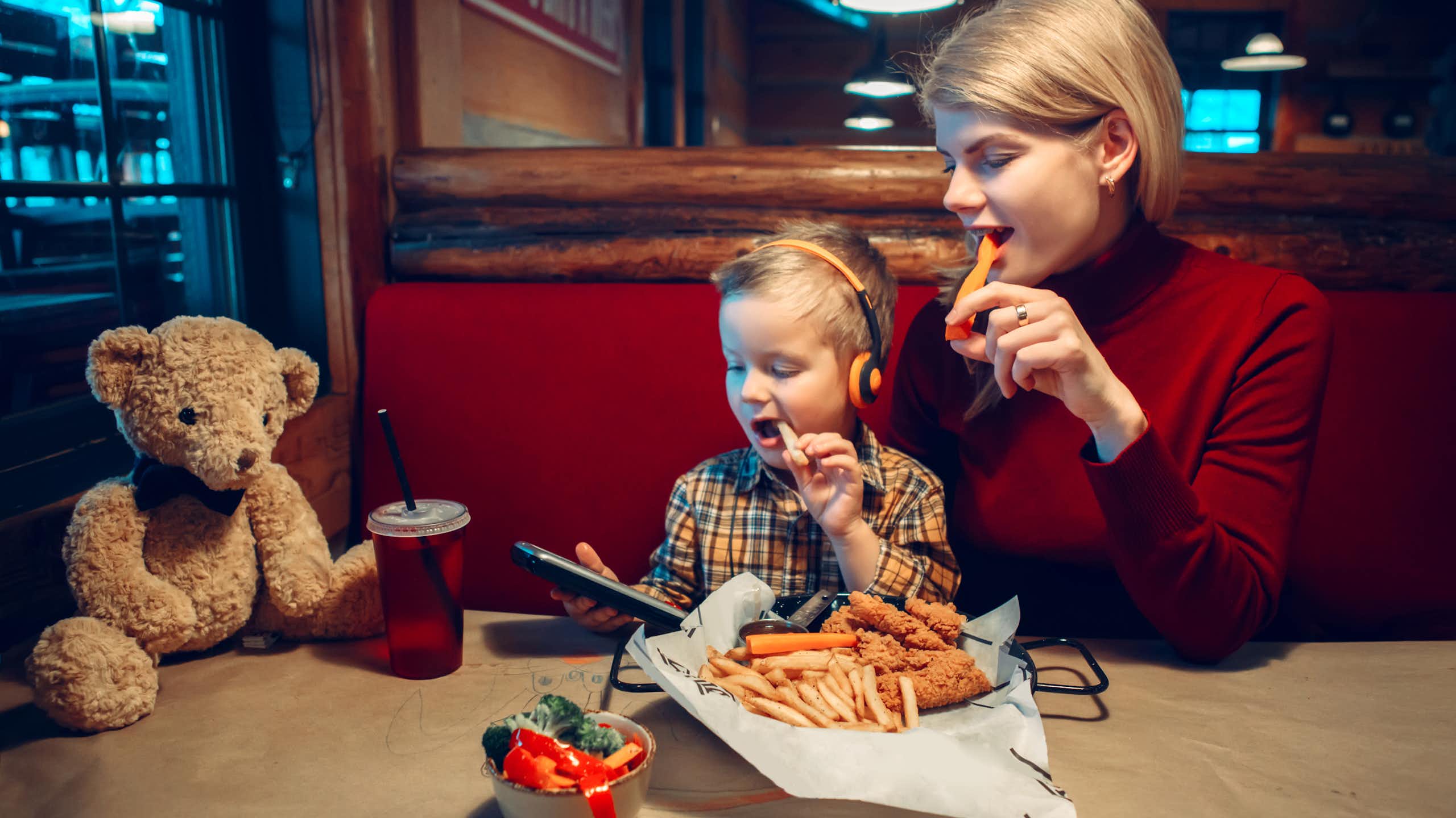 Mujer y niño comiendo en un restaurante mientras miran la pantalla de un dispositivo.