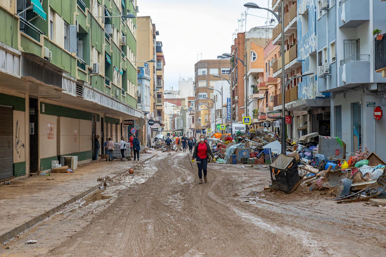 Una calle llena de barro y escombros con una mujer y personas al fondo.