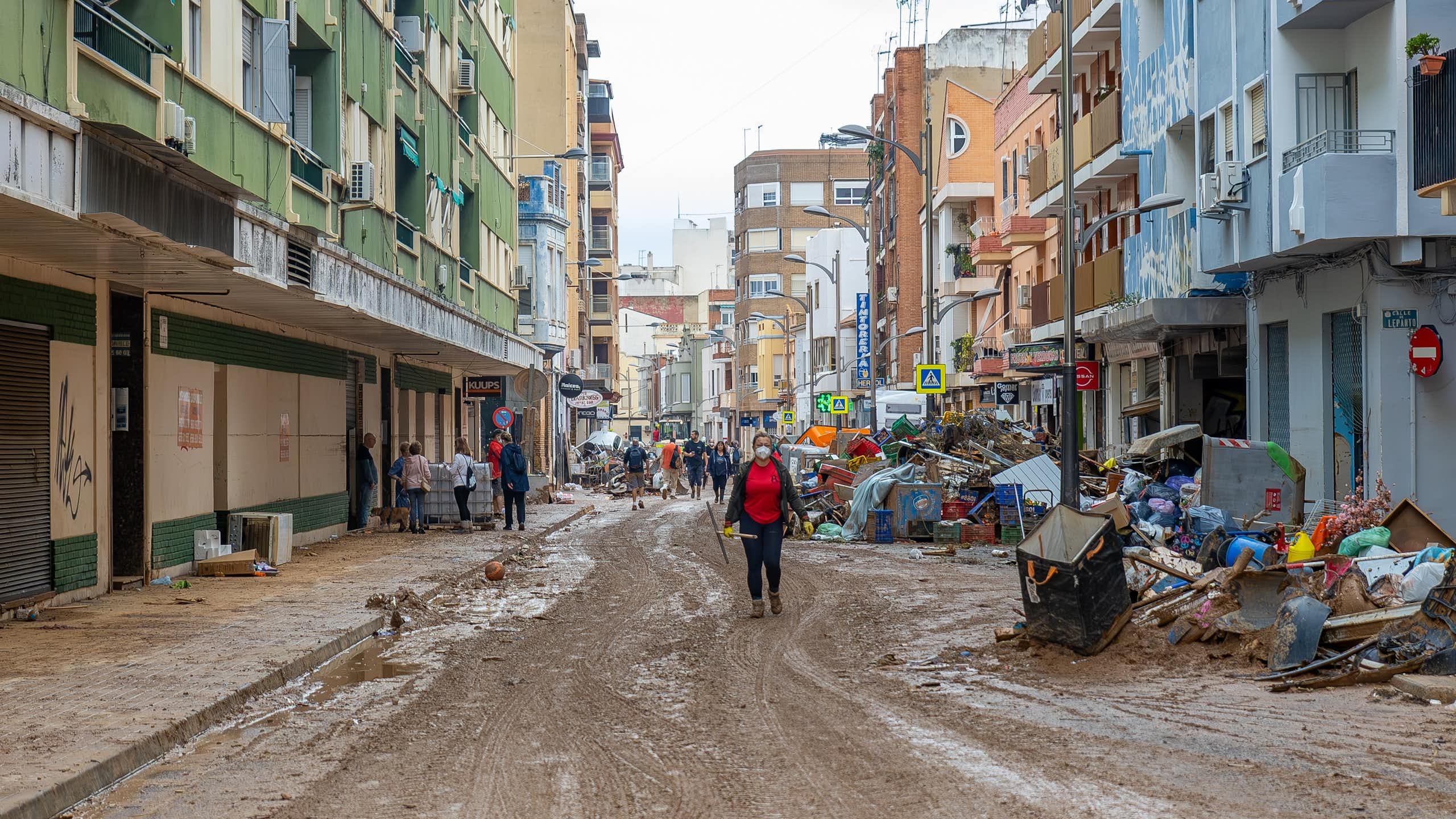 Una calle llena de barro y escombros con una mujer y personas al fondo.