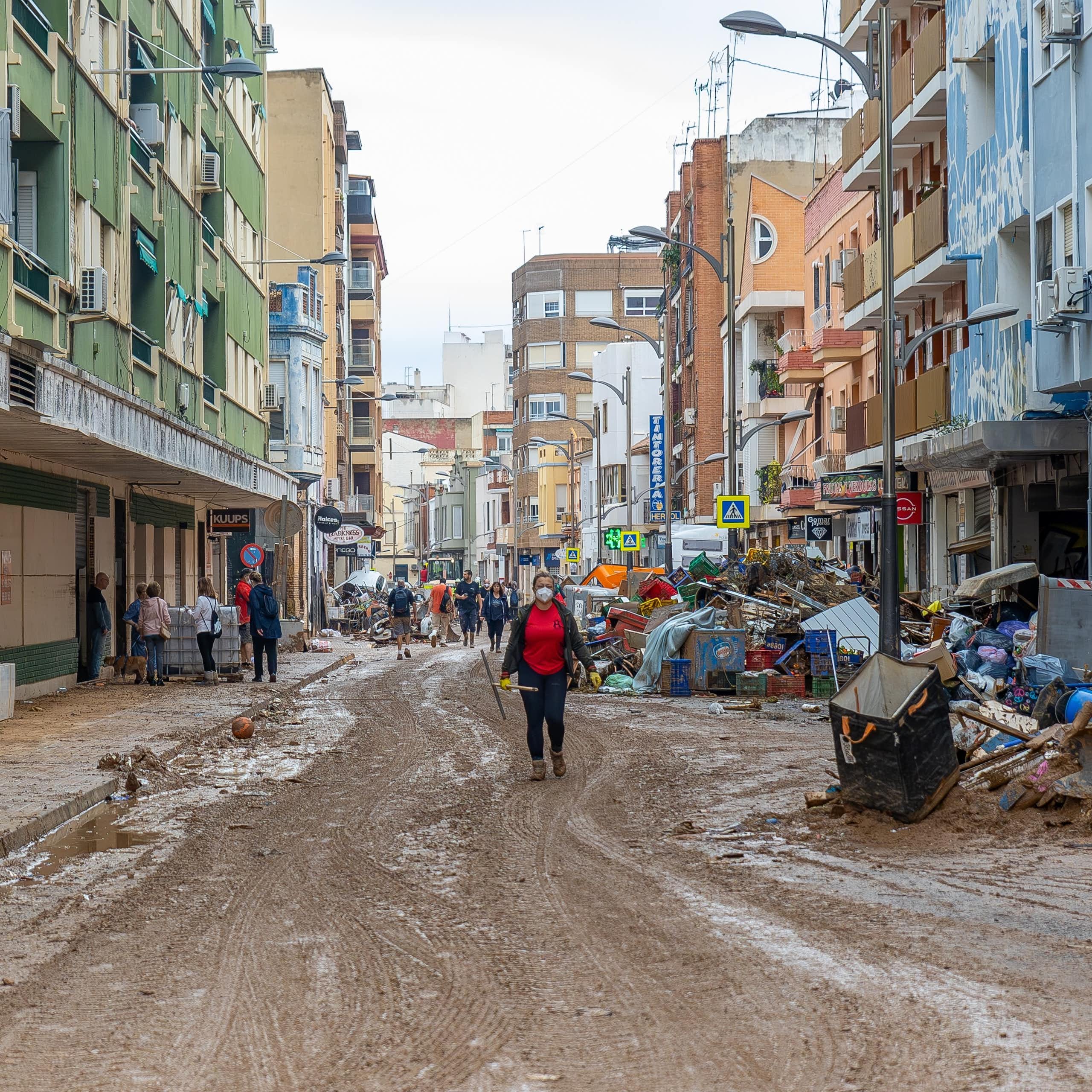 Una calle llena de barro y escombros con una mujer y personas al fondo.