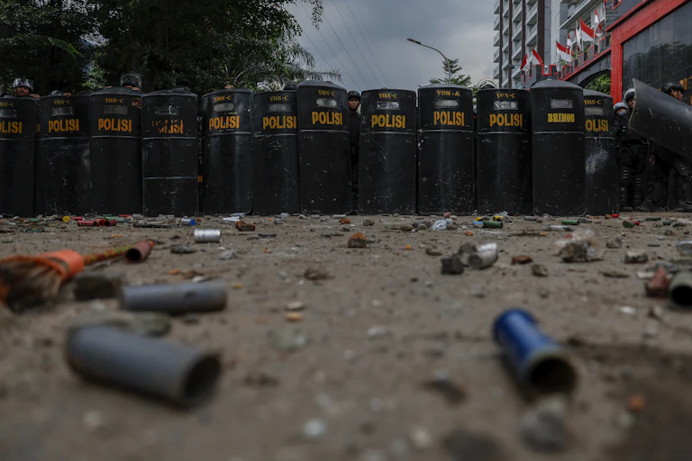 Indonesian riot police stand with their shields on a street littered with tear gas canisters.