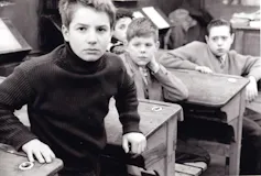 Un niño se levanta de un pupitre mientras sus compañeros le observan.