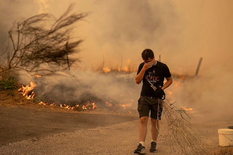 Un hombre compungido con en primer plano con incendio al fondo