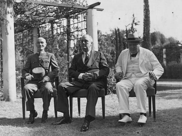 Three men sit in the sunshine wearing suits.