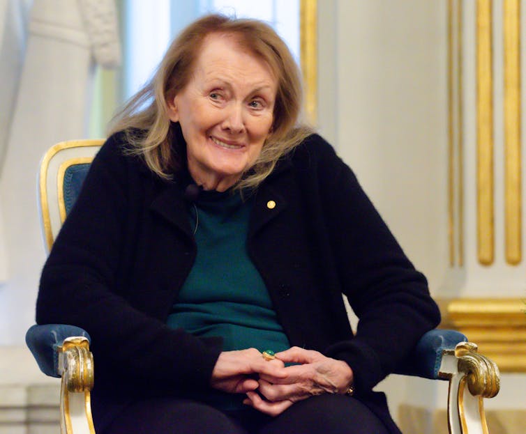 A fair-haired woman sits in an armchair.