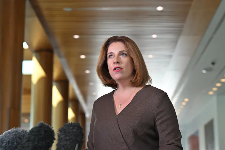A woman in business attire standing in front of a microphone.
