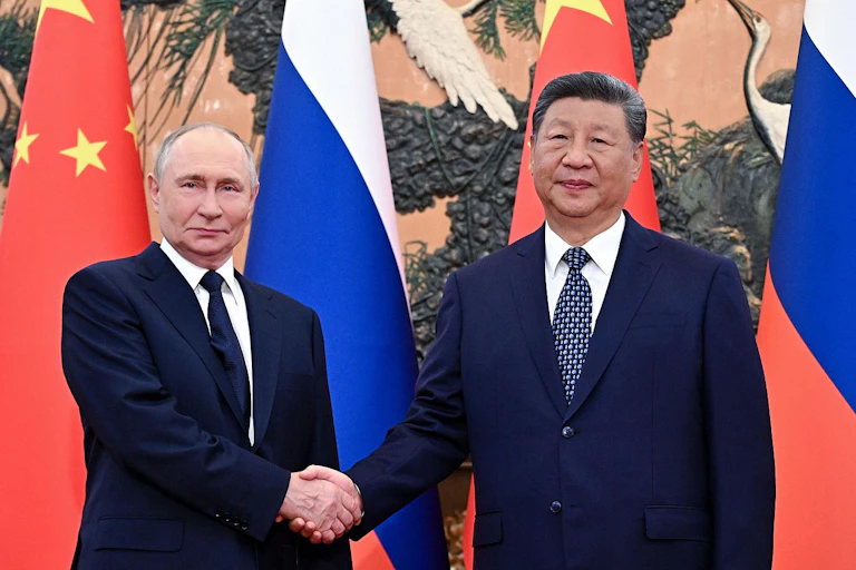 Xi Jinping y Vladímir Putin se dan la mano con banderas al fondo.