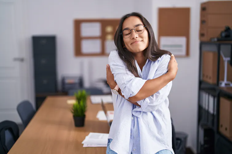 A young woman wearing glasses hugs herself.