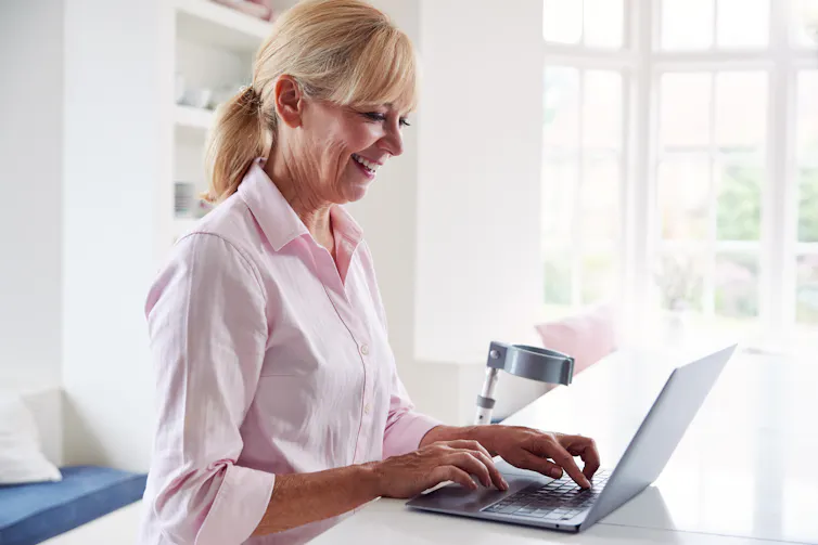 disabled woman working from home on her laptop with a walking aid beside her desk.
