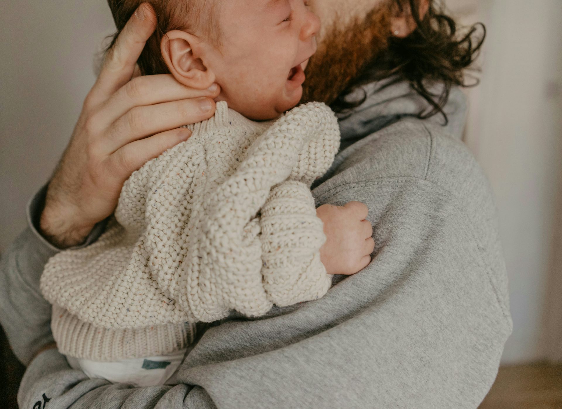 A man is holding a crying baby in his arms.
