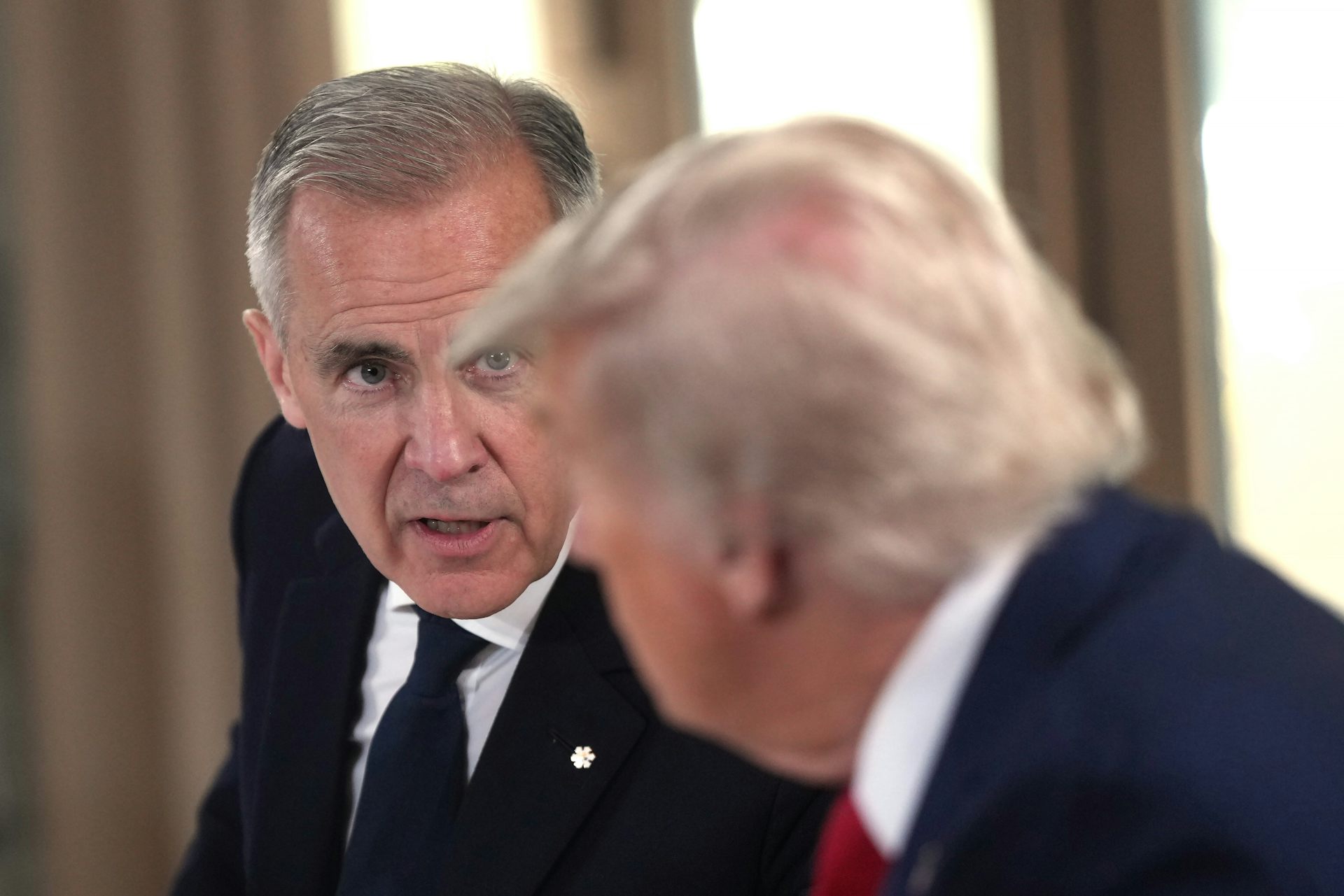 A man with short grey hair speaks to a man seen from behind with fluffy yellowish white hair.