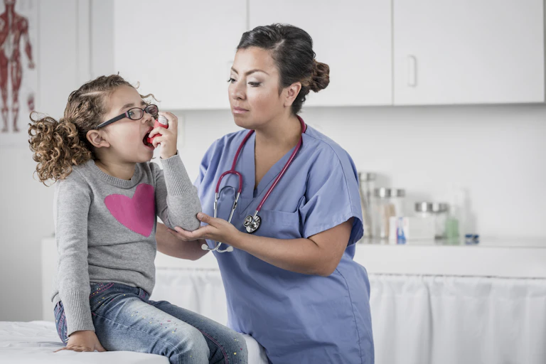 Nurse in blue scrubs helps little girl patient with asthma inhaler