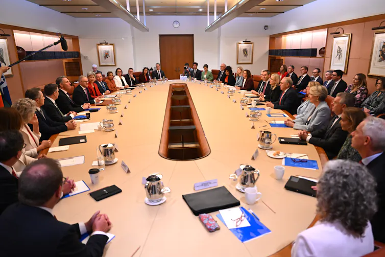 An aerial view of a large oval table surrounded by people having a meeting