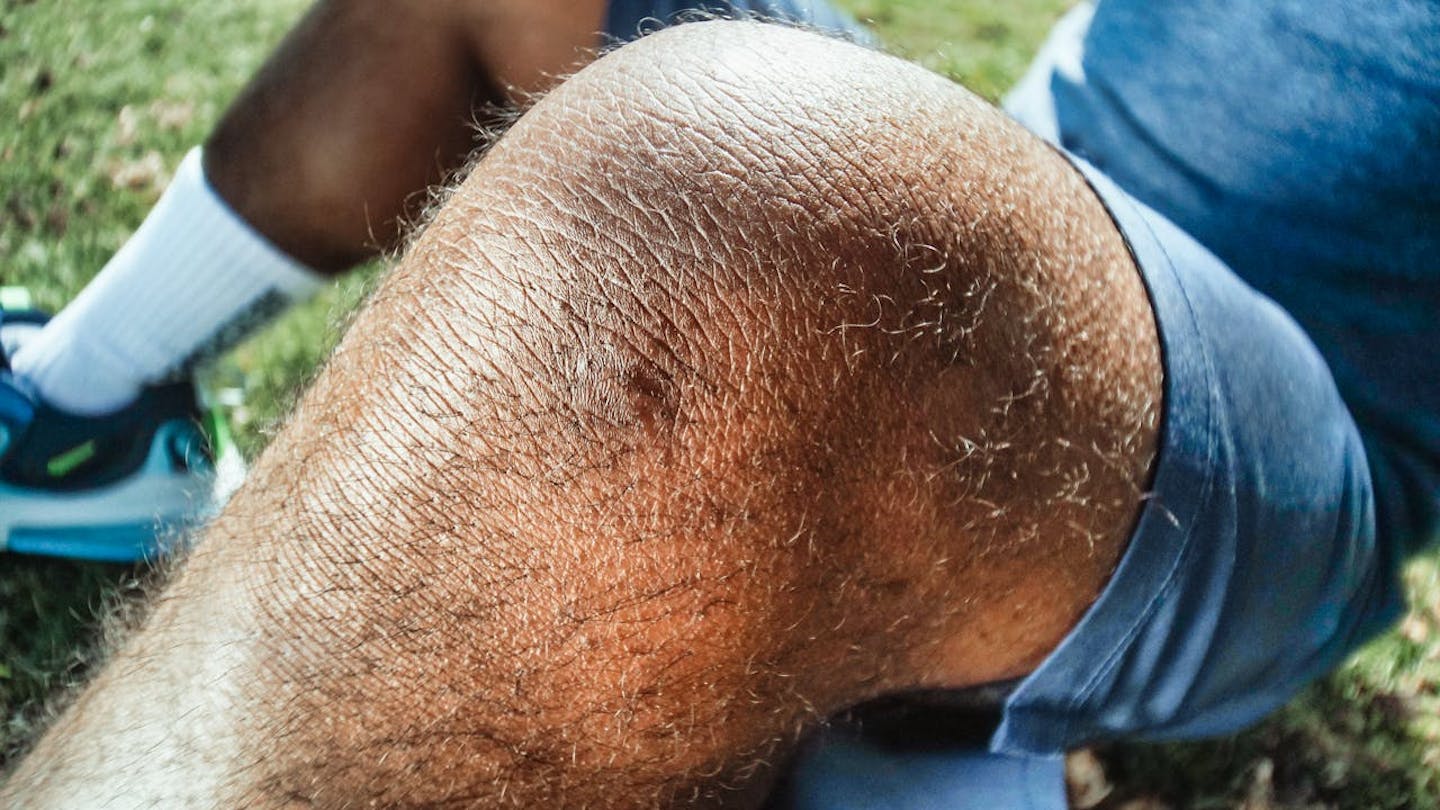 Man sitting on ground, close-up of bare knee.
