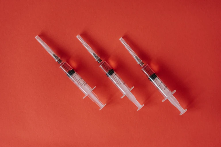 Three vaccine syringes placed diagonally on red background.