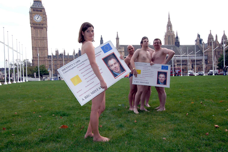 A group of naked people holding huge ID cards in front of Big Ben.
