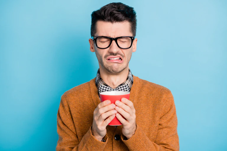 A man looking disgusted by what he is drinking.