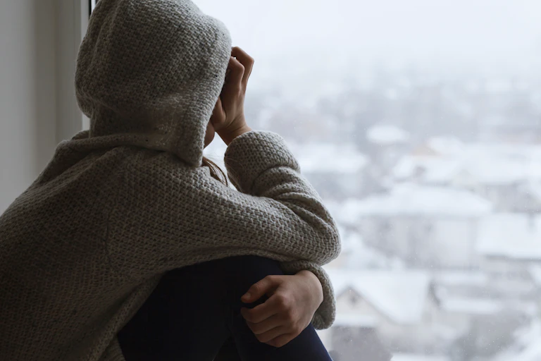 Upset sad teen looks out the window with back to the camera.