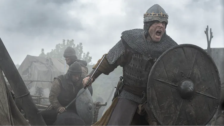 A scene from a medieval battlefield with a man in armour with a shield and a drawn sword.