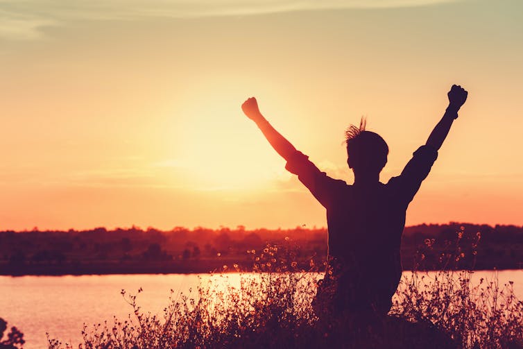 Young person raising arms to sky silhouetted against a sunset