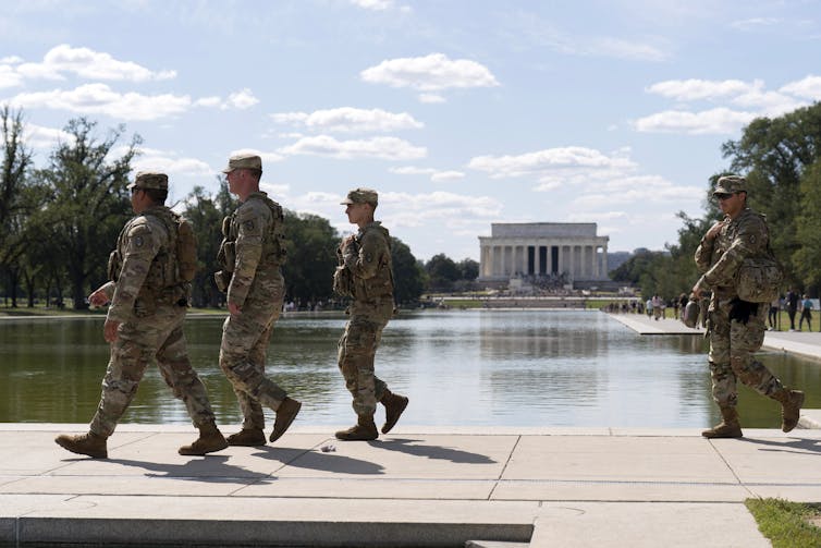 Four soldiers walk along a pool.