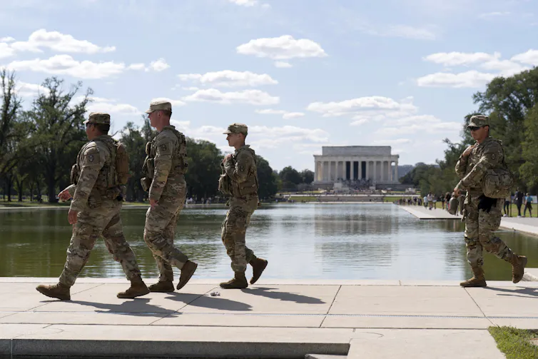 Four soldiers walk along a pool.