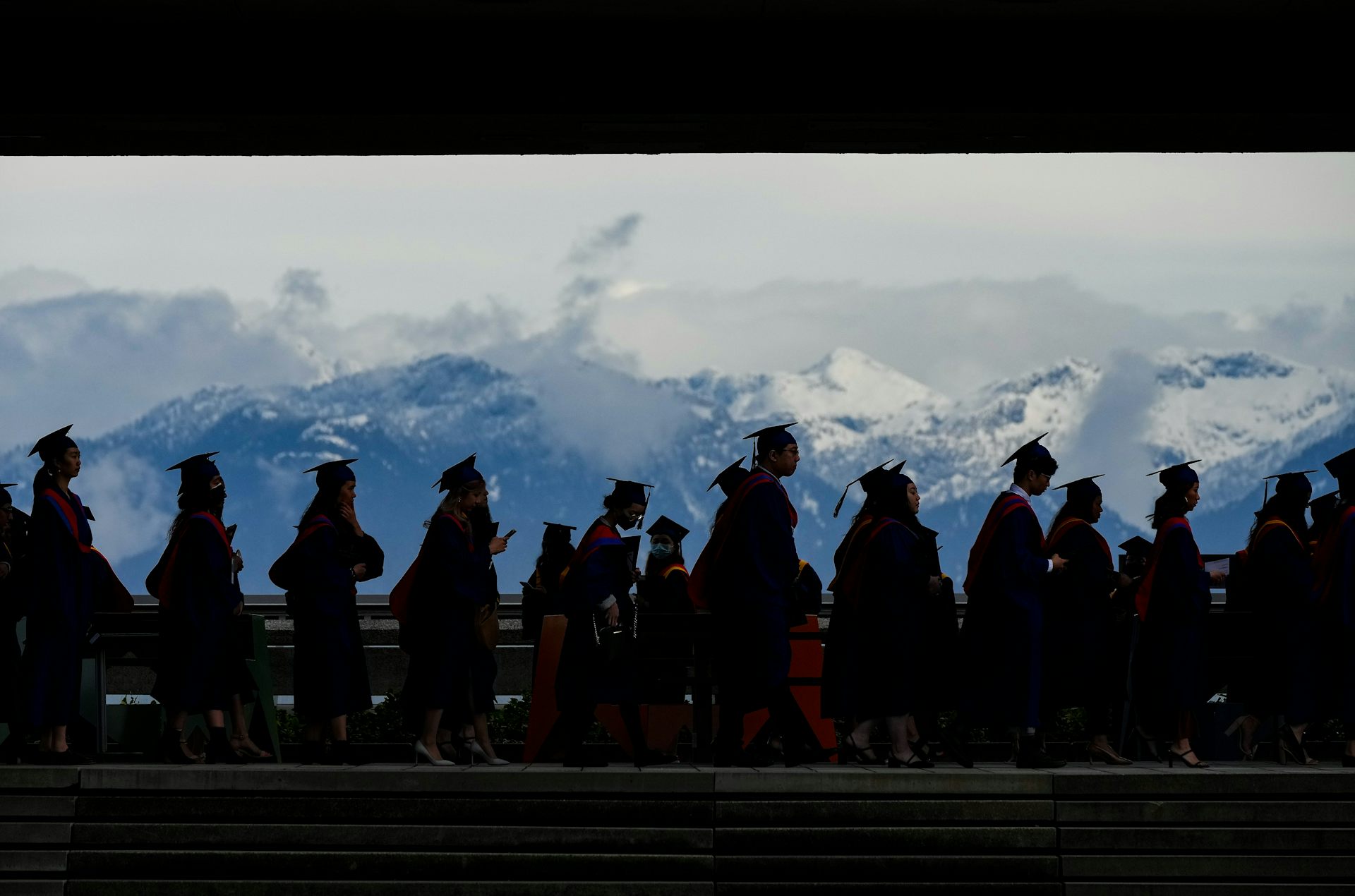 People in graduate caps and gowns silhouetted against a mountain vista.