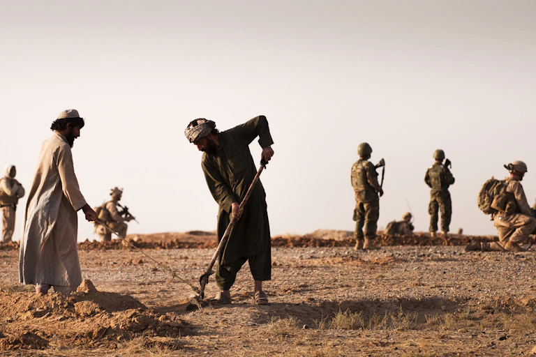 Afghan farmers plough a field with US soldiers in the background.